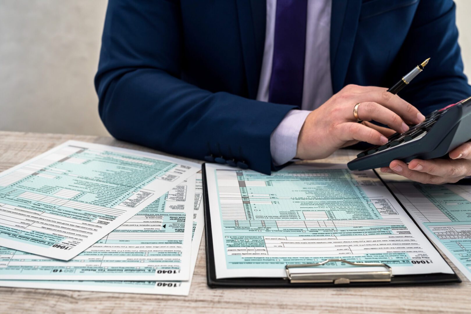 Person calculating taxes with forms and calculator.